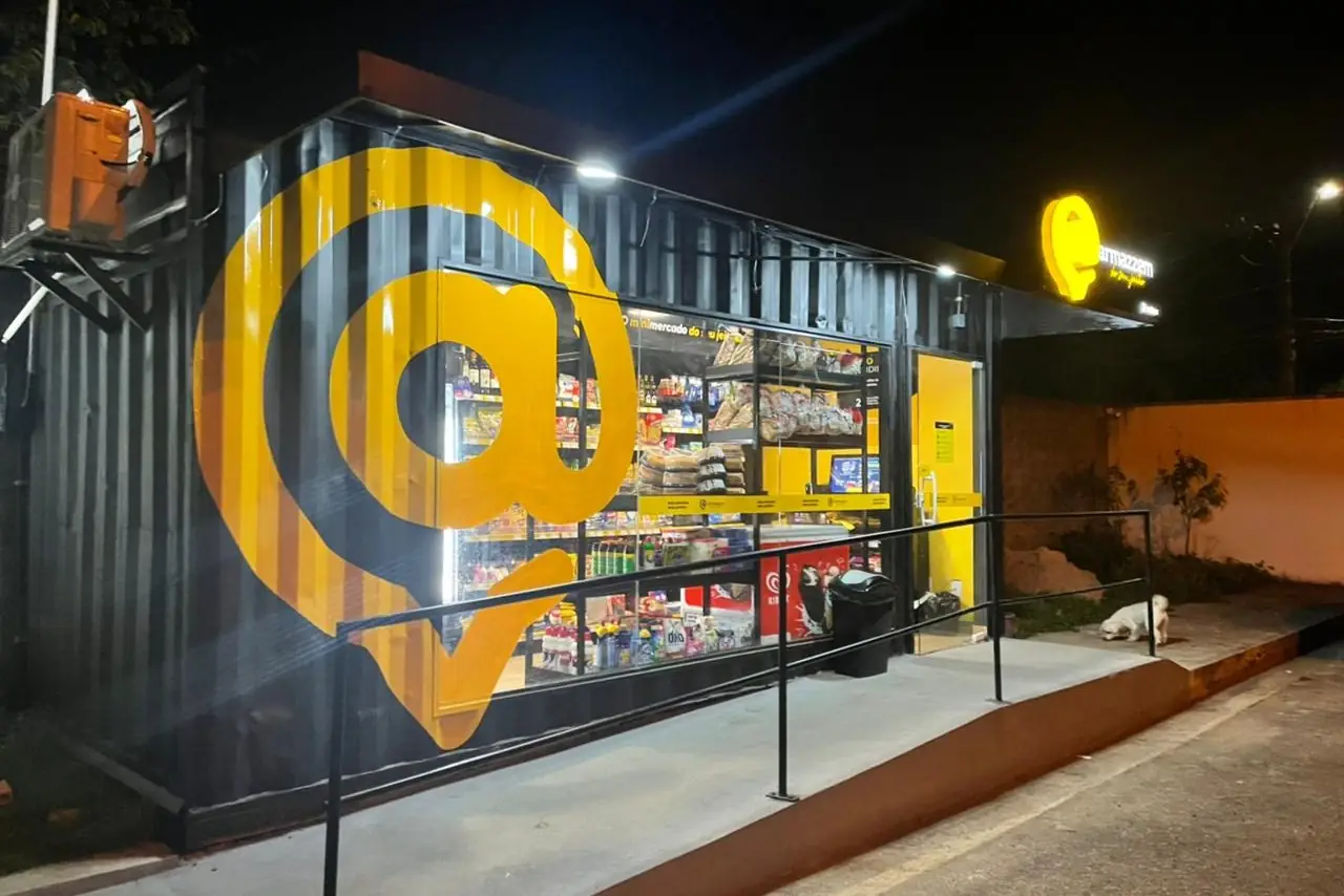 Loja container Armazzem acesa à noite, com o @ amarelo gigante na lateral